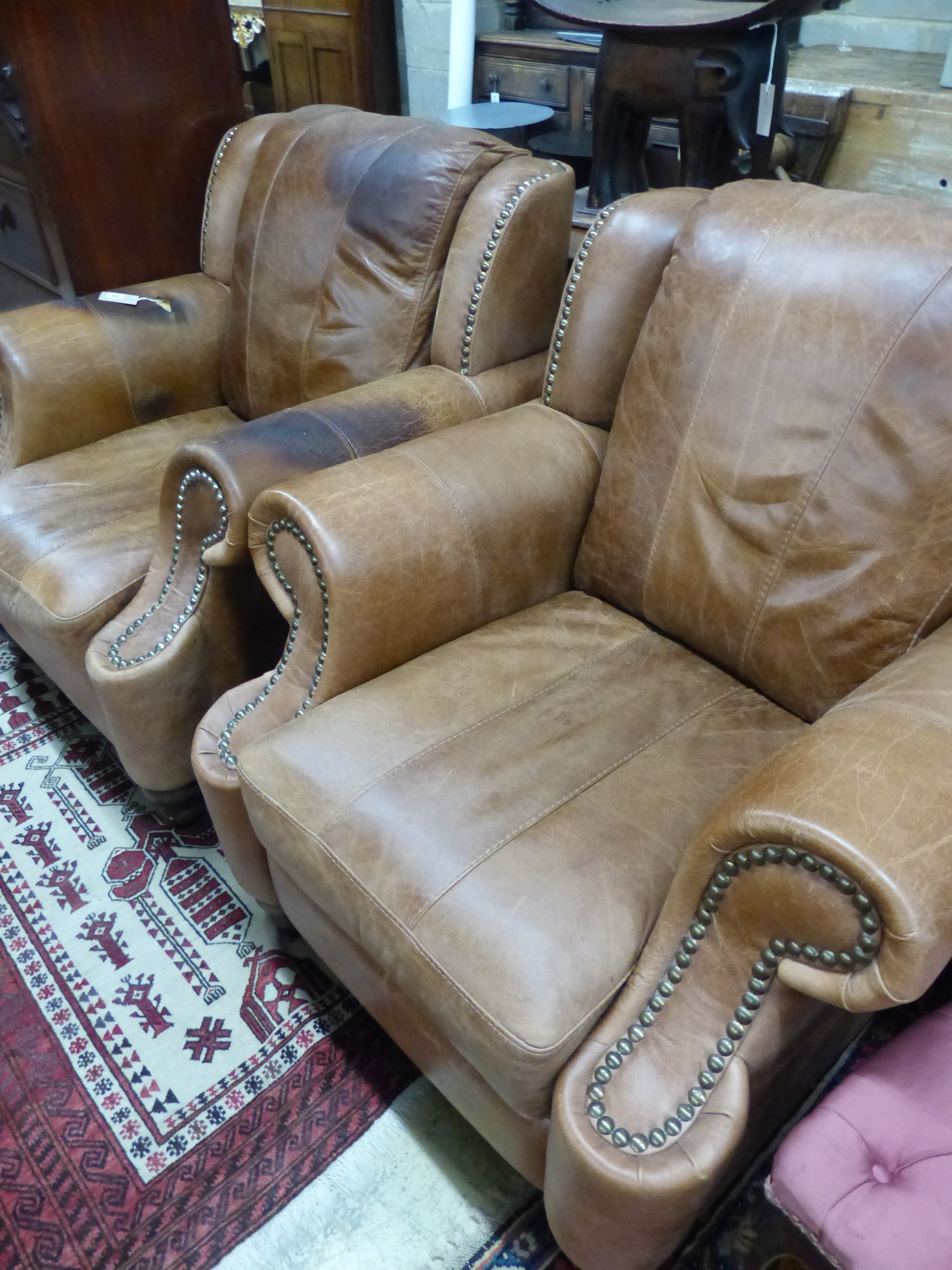A pair of tan leather armchairs, W.94cm D.94cm H.90cm (one arm holed)